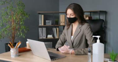 Maskeli ve lastik eldivenli şık, beyaz bir kadın dizüstü bilgisayarında video kaset takıyor, ofisinde oturuyor. Genç iş kadını web kamerasıyla konuşuyor ve görüntülü sohbet ediyor. İnternet işi.
