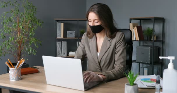 Ung sjuk kaukasisk affärskvinna i mask och gummihandskar skriva på tangentbordet och arbeta på bärbar dator. Ohälsosamt trött kvinnlig kontorsarbetare som skrattar och har hög temperatur. Coronavirus. — Stockvideo