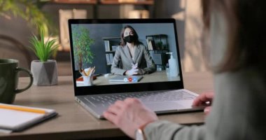 Kilitli maskeli kadın patronla çevrimiçi iş görüşmesi yapan bir kadın. İş kadını ofiste kabinede otururken çalışanla görüntülü konuşma yapıyor. Görüntülü konuşma. Karantina konsepti