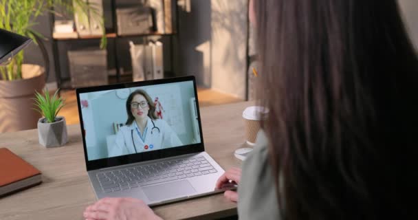 Γυναίκα έχει online βίντεο διαβούλευση με Καυκάσια όμορφη γυναίκα γιατρό στο φορητό υπολογιστή. Όμορφη γιατρός μιλάει με το κορίτσι σε τηλεδιάσκεψη και δίνει τον αντίχειρα επάνω, ενώ κάθεται στο νοσοκομείο. — Αρχείο Βίντεο