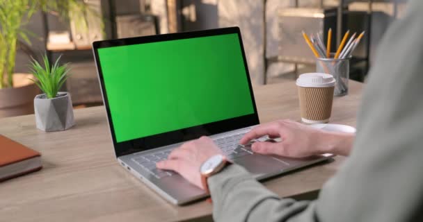 女人坐在办公桌前的房间里，用绿色屏幕在笔记本电脑上打字。自由撰稿人在电脑上用彩色按键敲击和发短信。在笔记本电脑上工作的女性手。工作概念 — 图库视频影像
