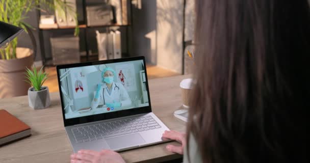 Doctor en traje de protección en máscara hablando con paciente femenina en videoconferencia. Chica hablando con el médico a través de la webcam portátil y la celebración de guantes de protección en la habitación. Concepto de cuarentena — Vídeos de Stock