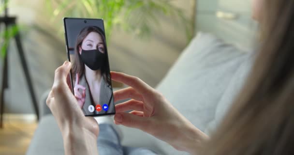 Γυναίκα έχει online συνομιλία βίντεο στο smartphone με όμορφη γυναίκα στη μάσκα. Επιχειρηματίας που μιλάει σε βίντεο chat με υπάλληλο ενώ κάθεται στο γραφείο. Βίντεο από το σπίτι. Έννοια κλειδώματος — Αρχείο Βίντεο