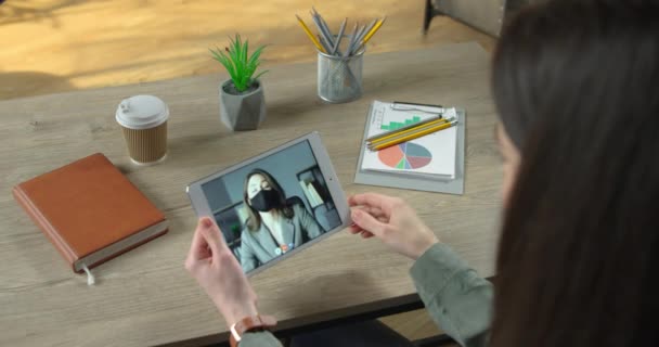 Üzletasszony beszél videóhíváson táblagépen az alkalmazottal, miközben az irodai szekrényben ül lezárva. Egy nő online tanácskozik a női főnökkel maszkban. Videó chat. Karantén elve — Stock videók