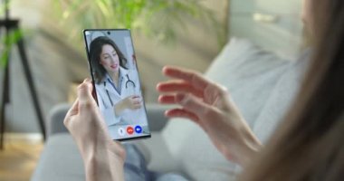Kafkasyalı doktorla tıbbi maske hakkında video görüşmesi yapan bir kadın. Güzel bir bayan doktor akıllı telefondan yüz maskesi takmayı öğretiyor. Virüs konsepti