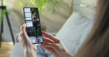 Kız evde dinleniyor ve kaslarını ısıtan beyaz kadın fitness eğitmeniyle cep telefonunda video görüşmesi yapıyor. Karantina Spor Konsepti 'nde bir kadın video konferansında antrenman izliyor.