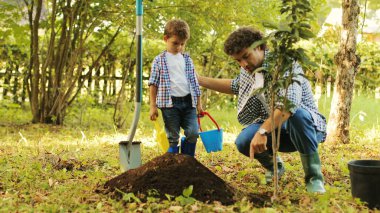 Küçük bir çocuk ve babasının ağaç dikerken ki portresi. Adam kovadan ağacı alıp deliğe sokuyor. Sonra ortaya çıktı ve oğluna bir şey açıkladı. Sonra gülümserler. Bulanık arkaplan