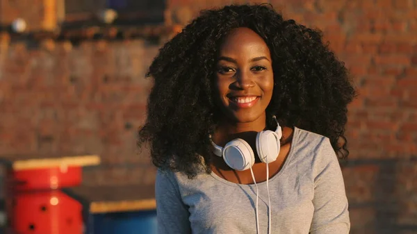 Detail portrét atraktivní kudrnaté vlasy africké ženy se sluchátkem na krku s úsměvem na fotoaparátu. — Stock fotografie