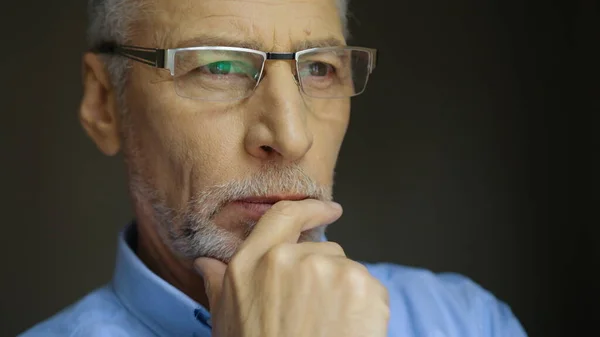 Close up retrato de um velho sério com barba cinzenta nos óculos olhando para a janela. Retrato de visão lateral . — Fotografia de Stock