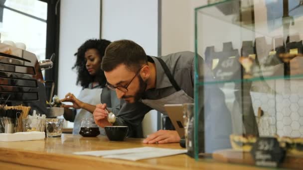 Hipster kaukasischer Barista mit Bart und afrikanischer junger Frau, die in einem modernen trendigen Café arbeitet, Frau wäscht Tasse und Mann schnuppert frischen Kaffee. — Stockvideo