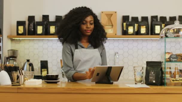 Kahverengi kıvırcık saçlı, tablet kullanan, kameraya bakıp kahve kafesinde gülümseyen Afrikalı kadın portresi.. — Stok video