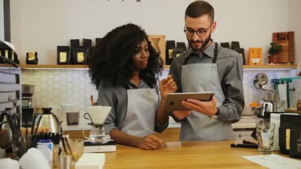 Retrato de un joven empresario propietario masculino mostrando a una empleada africana nuevo menú de café en la tableta durante el día de trabajo . — Vídeos de Stock