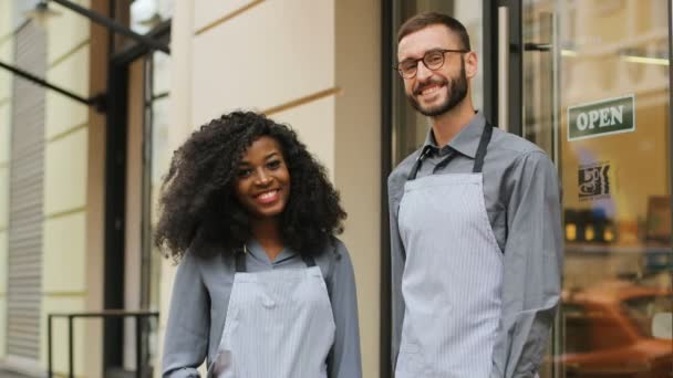 Portrait of female and male waiters hugging and smiling on camera outside of the modern cafe door. — Stock Video