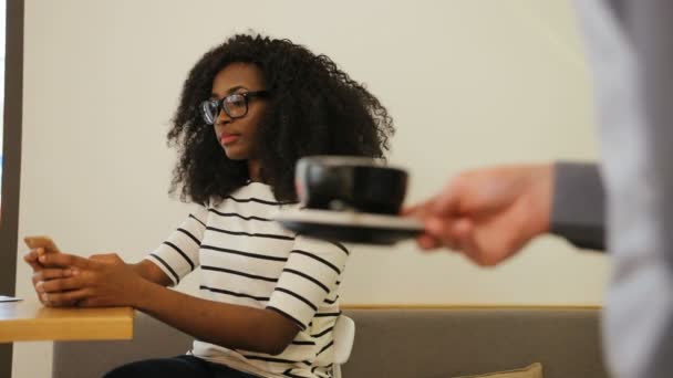 Close up tiro de garçom caucasiano mãos aserving a xícara de ordem de café para a jovem mulher africana beatiful no café elegante . — Vídeo de Stock