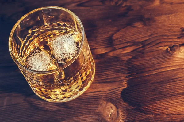 Parte superior de la vista de whisky en vidrio con cubitos de hielo sobre fondo de mesa de madera — Foto de Stock