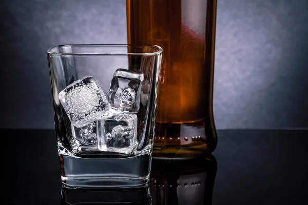 Nahaufnahme von Whisky mit Eiswürfeln im Glas nahe der Flasche auf schwarzem Hintergrund, kalte Atmosphäre — Stockfoto