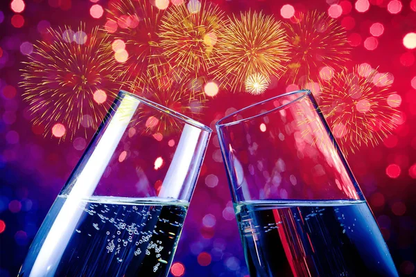Champagne flutes with golden bubbles on red and purple light bokeh and fireworks sparkle background — Stock Photo, Image