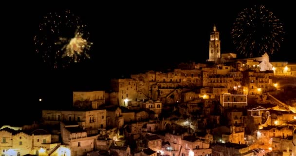 Панорамный вид на типичные камни (Sassi di Matera) и церковь Матера ночью, с золотым абстрактным мигающим сверкающим фейерверком празднования фейерверк свет, с новым годом — стоковое видео