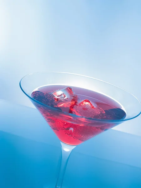 red cocktail drink with ice cubes on blue light tint background, fun and dance disco