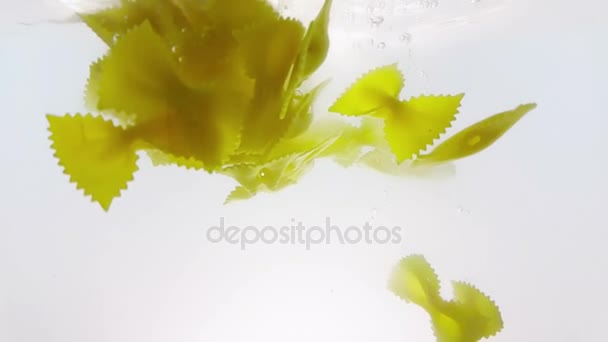 Salpicadura de pasta farfalle cayendo en agua hervida, disparado en cámara lenta sobre fondo blanco, nutrición y salud — Vídeo de stock