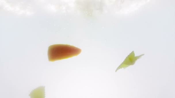 Pasta farfalle y salpicadura de rodaja de tomate cayendo en agua hervida, disparado en cámara lenta sobre fondo blanco, nutrición y salud — Vídeo de stock
