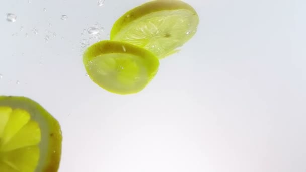 Salpico de frutas de fatia de limão caindo em coquetel de álcool branco e copo de água, filmado em câmera lenta no fundo branco, diversão, nutrição e bebida — Vídeo de Stock