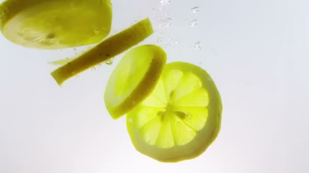Lemon slice owoce plusk spada w dół do biały koktajl alkoholu i wody pitnej szkła, strzał w zwolnionym tempie na białym tle, zabawa, odżywianie i picie — Wideo stockowe
