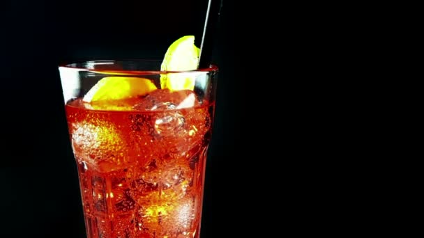 Снимок в замедленной съемке питьевого стакана апельсинового коктейля с кубиками льда, с шипучими пузырьками движения на черном фоне, праздники и летнее время — стоковое видео
