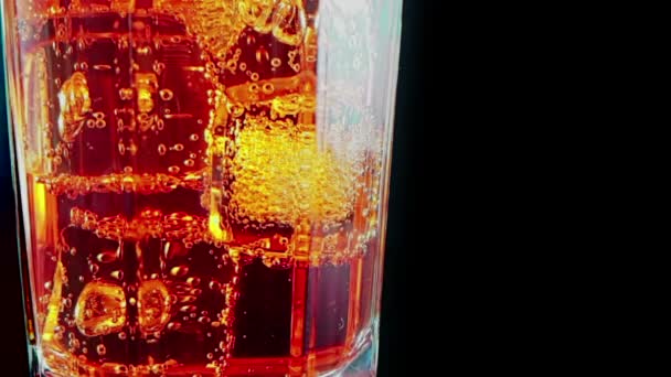 Знімок у повільному русі склянки питного аперитиву Скритца апельсинового коктейлю з кубиками льоду, з божевільними бульбашками руху на чорному фоні, свята та літній час — стокове відео