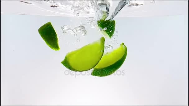 Éclaboussure de fruits en tranches de citron vert tombant dans un cocktail blanc et verre à boire de l'eau, tourné au ralenti sur fond blanc, amusant, nutrition et boisson — Video