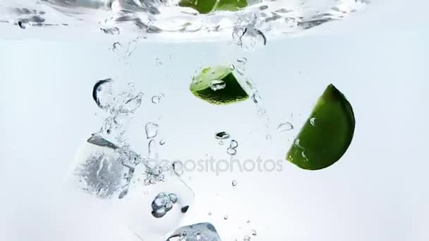 Frutta di calce e cubetti di ghiaccio schizzano giù in cocktail bianco e bicchiere di acqua potabile, girato al rallentatore su sfondo bianco, divertimento, nutrizione e bevande — Video Stock