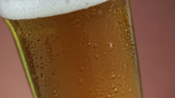 Frisches Bier mit Schaum in Glas mit gefrorenen Tropfen, auf goldbraunem Hintergrund, unterhaltsame und nahrhafte Speisen und Getränke — Stockvideo