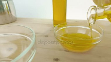 zeytinyağı şişesi yakınındaki ahşap masa arka plan üzerinde beyaz kap içinde şişede pişirme zeytinyağı dökme, beyaz arka plan, sağlıklı gıda beslenme kavramı üzerinde ağır çekimde atış 