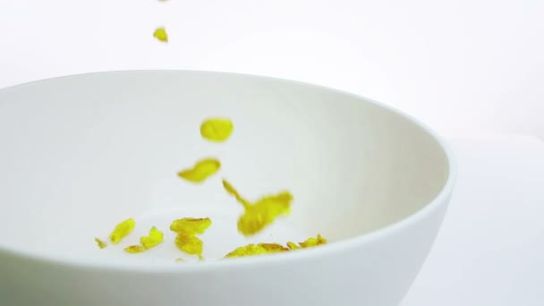 Хлопья кукурузы падают в миску, выстрел в замедленной съемке на белом фоне, концепция диеты здоровой пищи — стоковое видео
