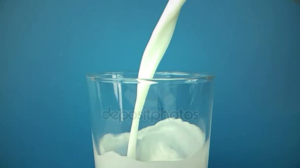 Fresh white milk pouring into drinking glass on blue background, shooting with slow motion, diet and healthy nutrition — Stock Video