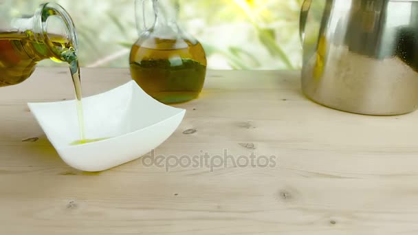 Derramamento de azeite de cozinha na garrafa no recipiente branco sobre fundo de mesa de madeira perto de garrafa de azeite, filmado em câmera lenta ao ar livre, conceito de dieta alimentar saudável — Vídeo de Stock