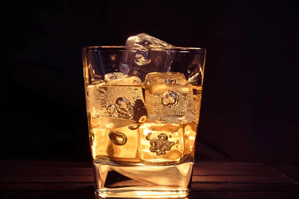 Vaso de whisky con cubitos de hielo sobre fondo oscuro y tabla de madera — Foto de Stock