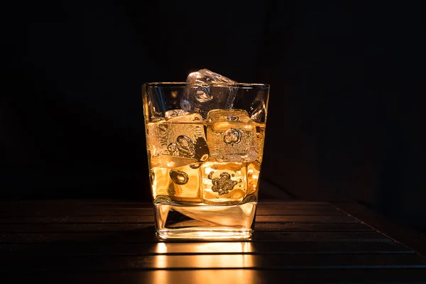 Whiskey with ice cubes in glass on dark background and wood tabl — Stock Photo, Image