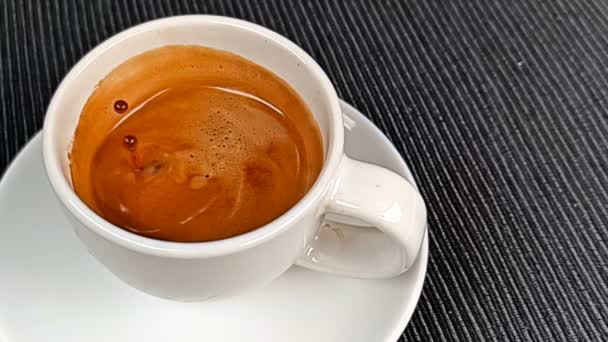 Капля кофе падает в замедленной съемке внутри чашки эспрессо итальянский кофе с пеной на черном фоне, еда и напитки — стоковое видео