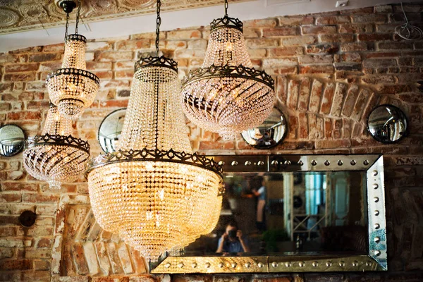 closeup view of cut-glass chandeliers hanging near brick wall indoors