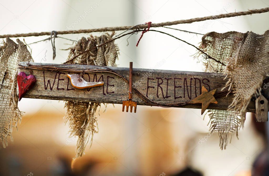 closeup daytime view of wooden sign with Welcome Friends words decorated with fabric and small objects