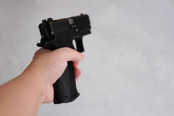 Woman holding gun in her hand at home. Focus hand of young women using black gun on gray background.