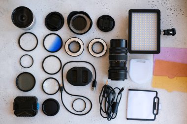 Grideki profesyonel fotoğrafçı için düz kompozisyon ekipmanı. Fotoğraf gradyan filtresi, makro halkalar, polarize filtre, şarj aleti, renkli plakalı video ışığı, kameralar için lens kapakları