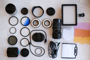 Grideki profesyonel fotoğrafçı için düz kompozisyon ekipmanı. Fotoğraf gradyan filtresi, makro halkalar, polarize filtre, şarj aleti, renkli plakalı video ışığı, kameralar için lens kapakları