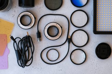 Grideki profesyonel fotoğrafçı için düz kompozisyon ekipmanı. Fotoğraf gradyan filtresi, makro halkalar, polarize filtre, şarj aleti, renkli plakalı video ışığı, kameralar için lens kapakları