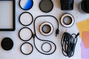 Grideki profesyonel fotoğrafçı için düz kompozisyon ekipmanı. Fotoğraf gradyan filtresi, makro halkalar, polarize filtre, şarj aleti, renkli plakalı video ışığı, kameralar için lens kapakları