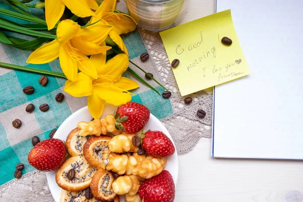 Coffee with sweets - pretzels with poppy seeds, fresh red strawberries and the inscription in the notebook. The view from the top space for your text. The concept of Breakfast for Valentine\'s Day