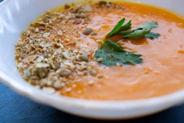 Mavi arka planda mor fesleğenli balkabağı çorbası ve kızarmış kabak çekirdeği. Manzara, yemek fotoğrafları, yemek tarifleri, dergiler