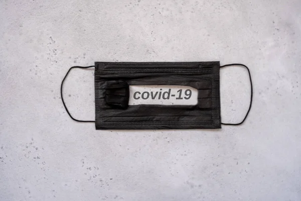 Máscara preta descartável de proteção médica com texto no slot covid-19 em cinza escuro. proteção de conceito de perigoso 2019-nCoV — Fotografia de Stock