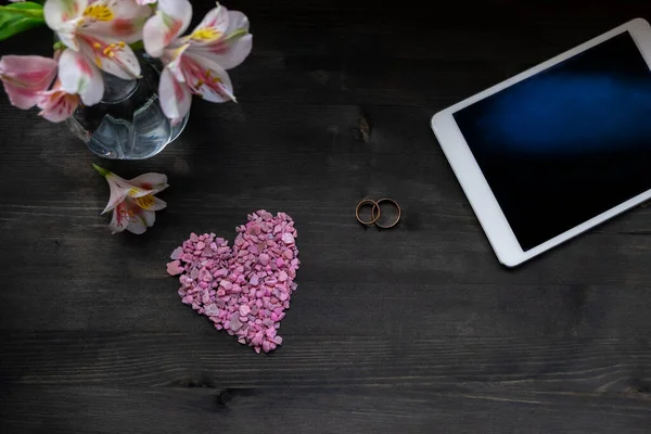 Sevgililer Günü geçmişi - pembe kalp, çiçekler, tablet ve alyanslar.